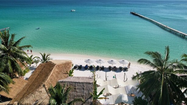 A beach with a long pier extending into the sea, a row of beach umbrellas, and palm trees. - White Sand Ark Resort (Koh Rong)