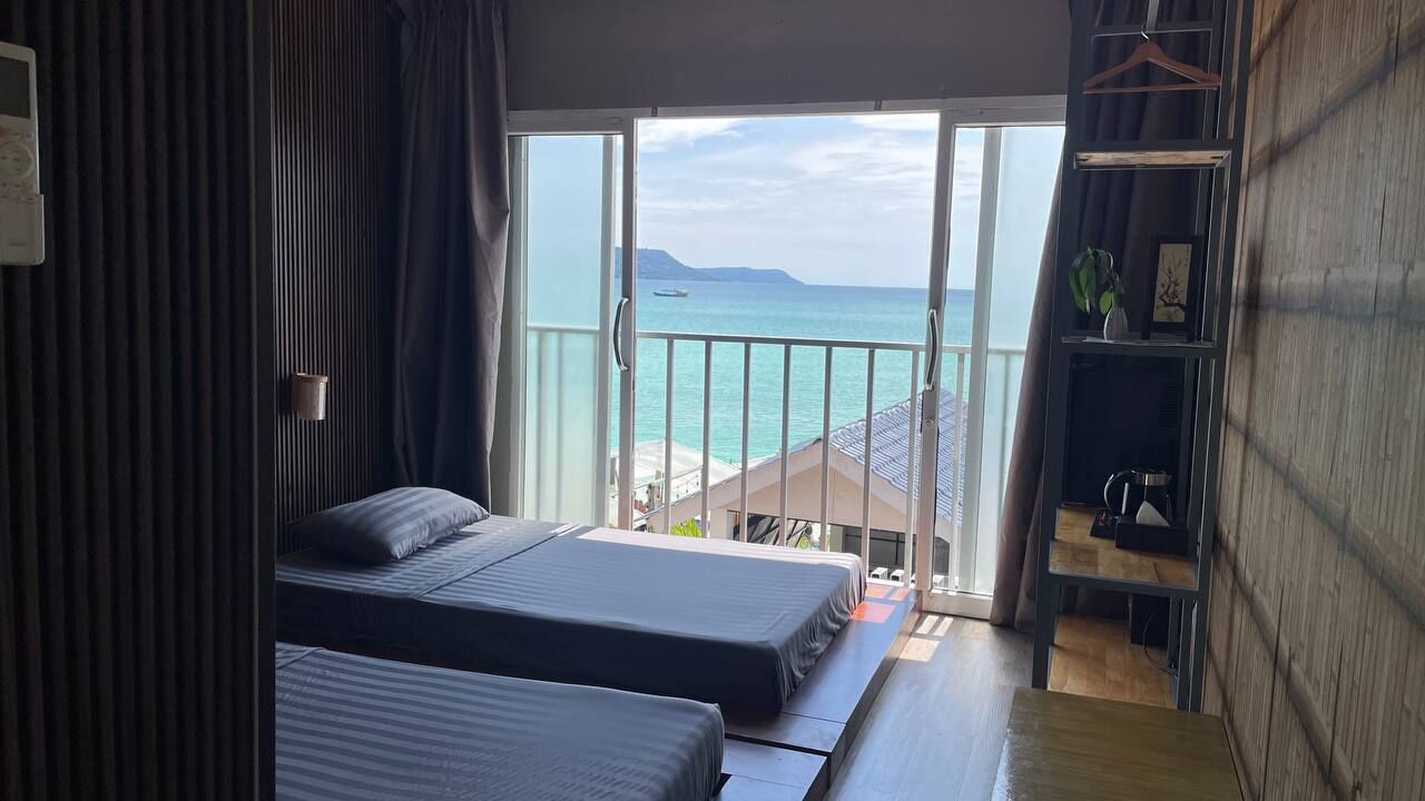 A room with two beds, a balcony with a view of the sea, and a wooden wall.