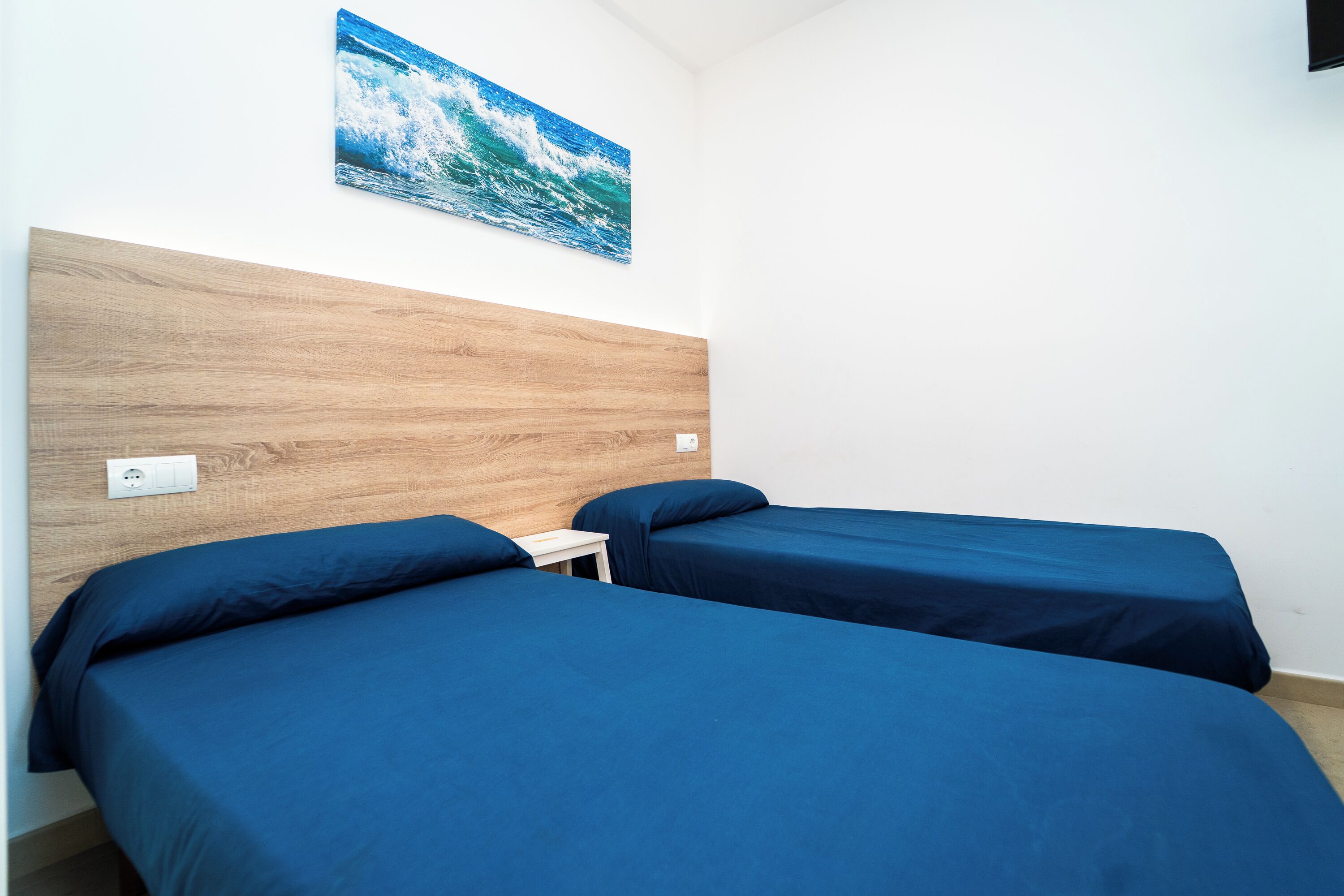 Een kamer met twee bedden, een houten hoofdbord, een klein tafeltje en een aan de muur hangend schilderij van een golf.