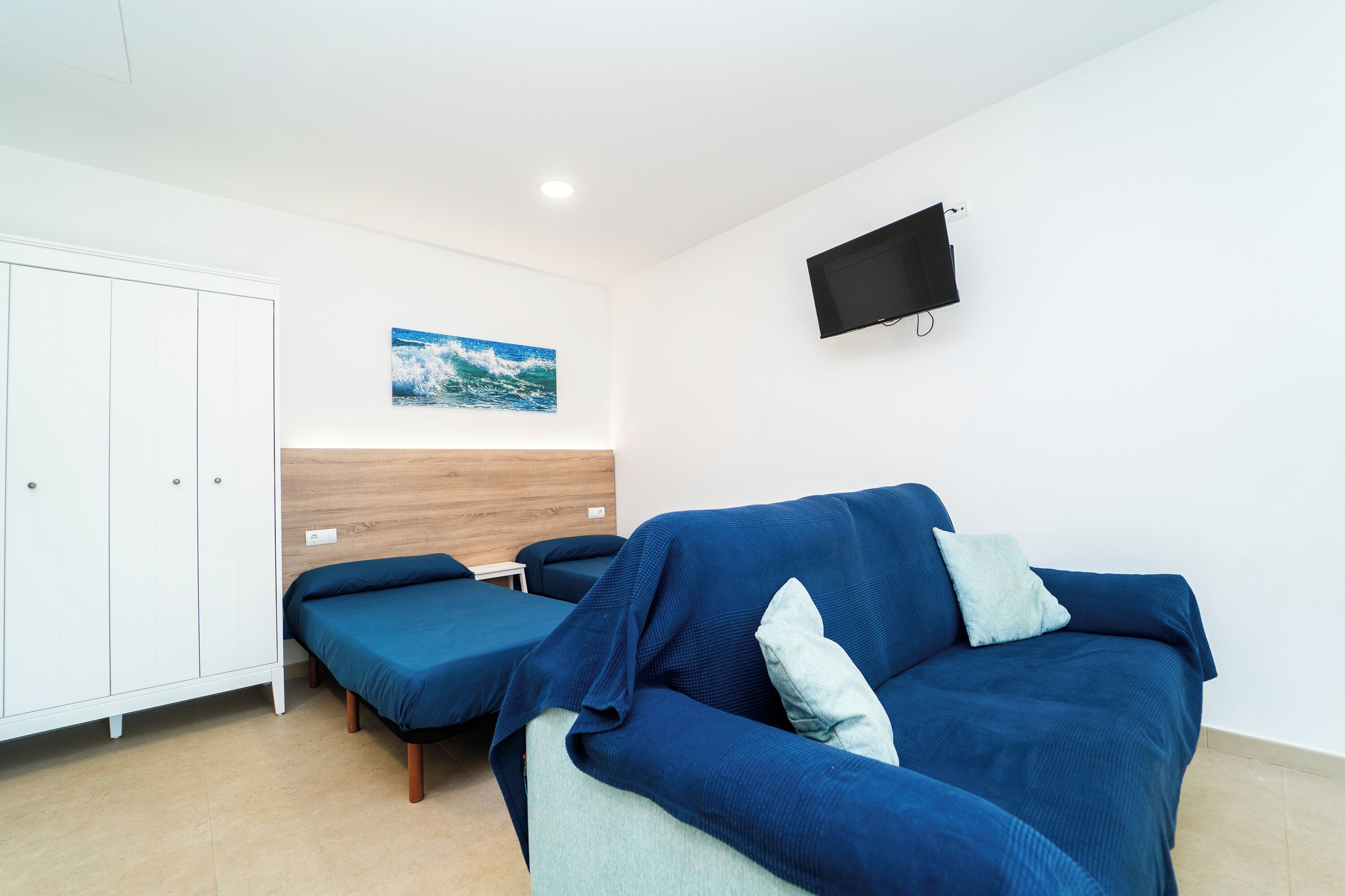 Ein Zimmer mit einem blauen Sofa, einem Bett, einem weißen Kleiderschrank und einem an der Wand befestigten Fernseher.