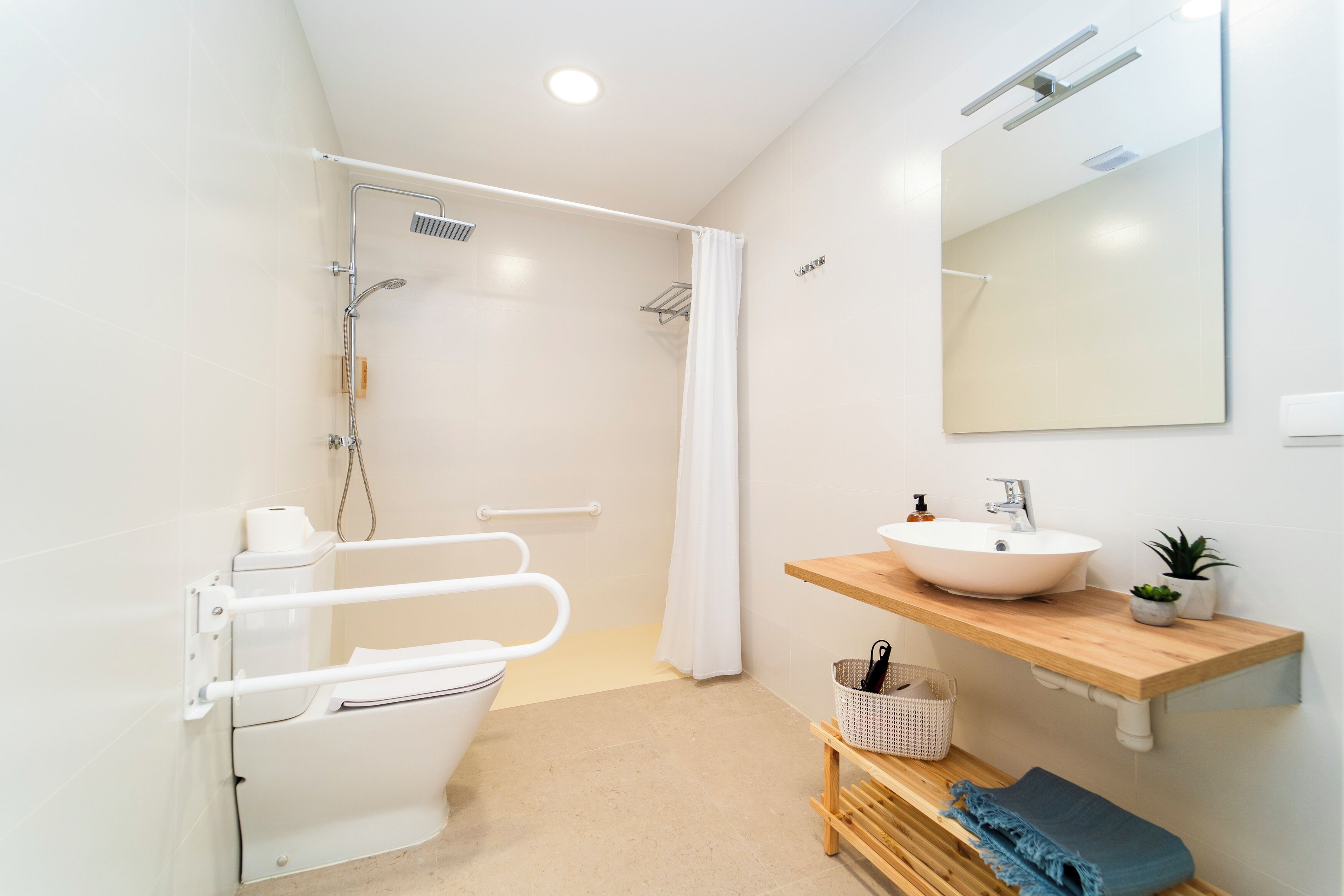 A modern bathroom with a white toilet, a shower with a glass door, a sink with a mirror above, and a wooden shelf with a plant.