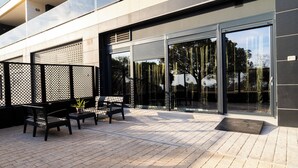 Un patio al aire libre con un conjunto de asientos, una planta en maceta y la fachada moderna de un edificio con grandes puertas de vidrio.