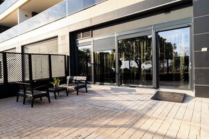 Un patio al aire libre con un conjunto de asientos, una planta en maceta y la fachada moderna de un edificio con grandes puertas de vidrio.