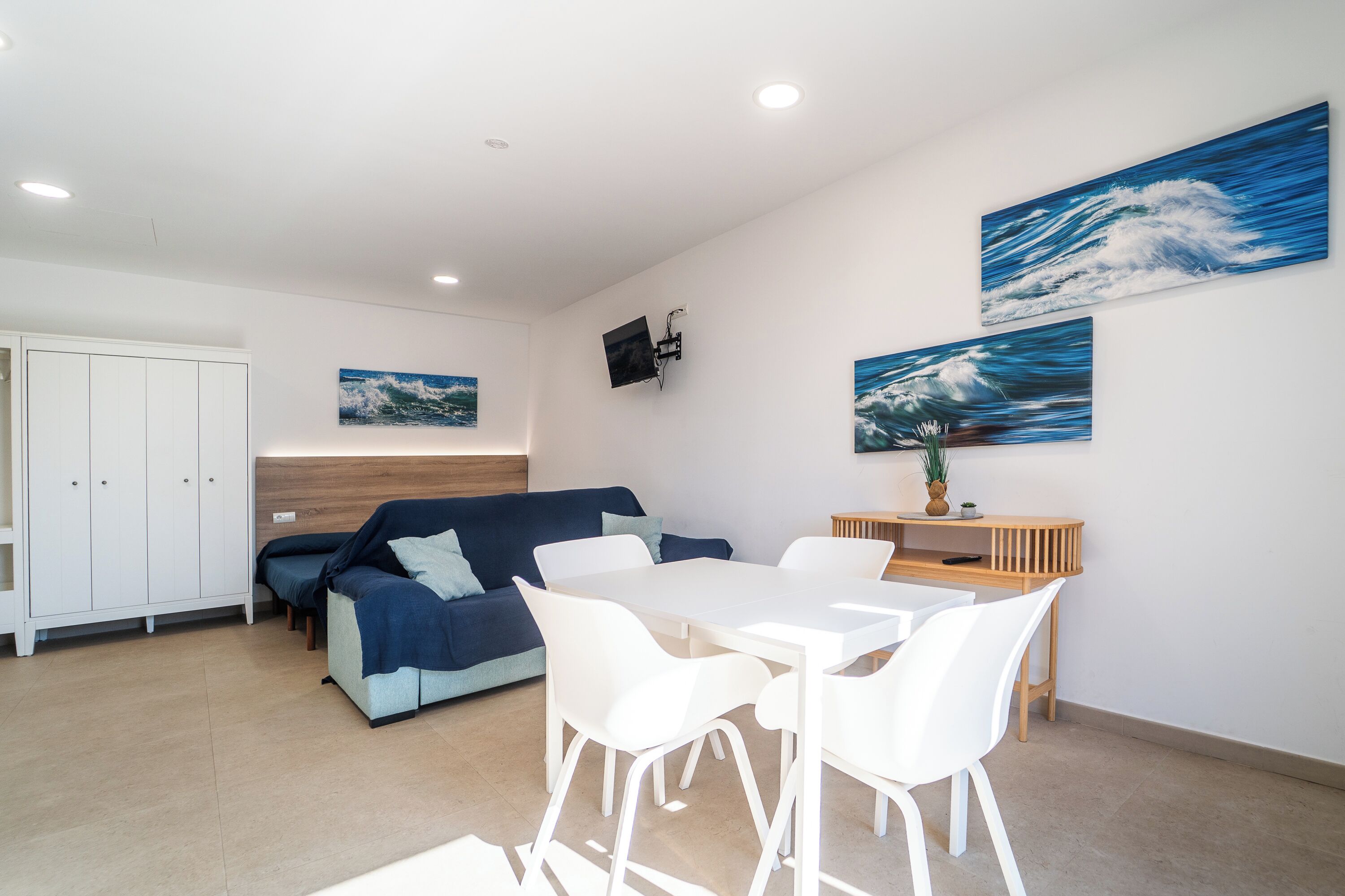 A modern living room with a sofa, a dining table with chairs, and artwork on the walls.