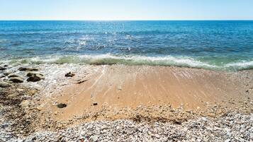 A beach with pebbles and sand, a clear blue sea, and a calm horizon.