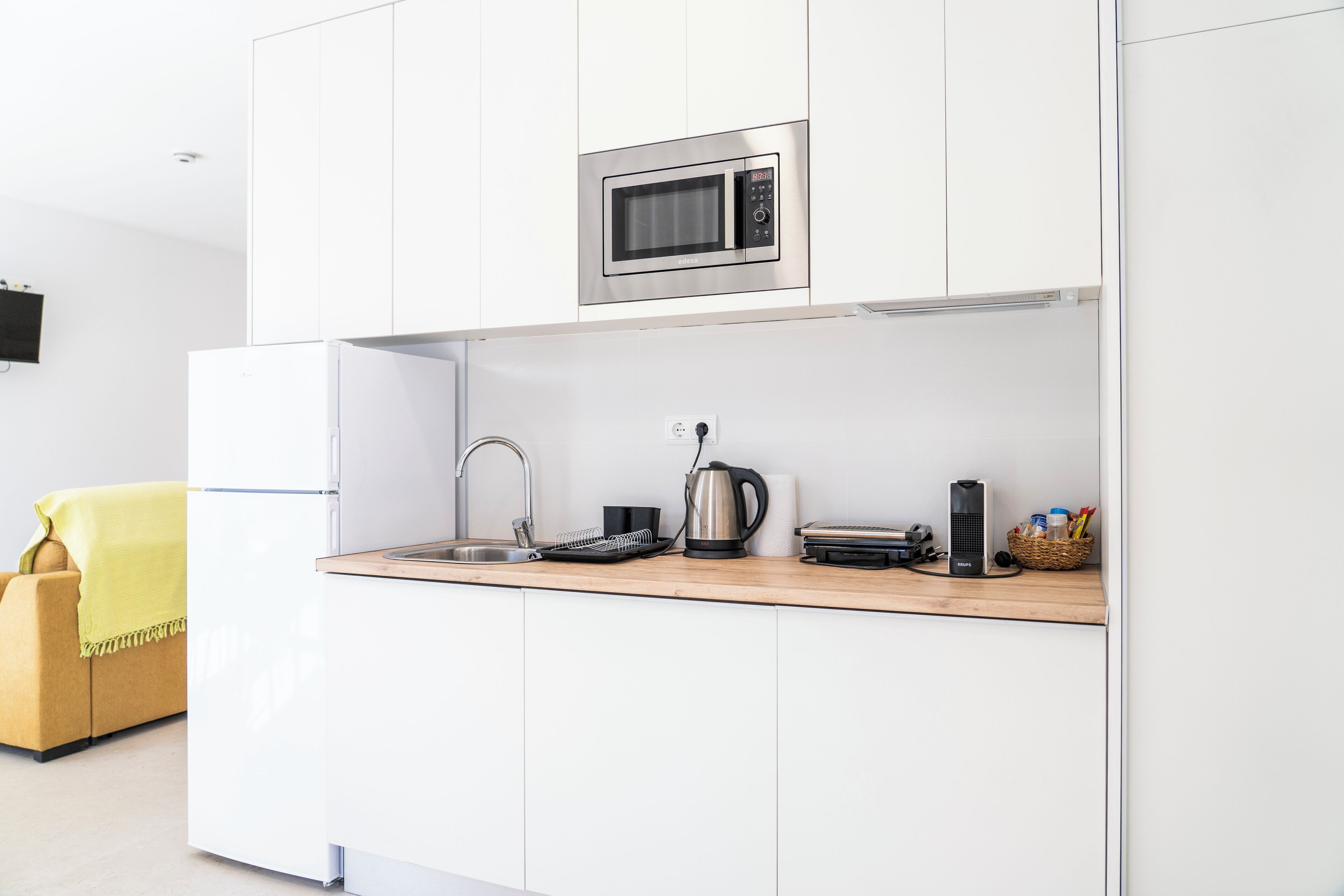 A modern kitchen with white cabinetry, a stainless steel microwave, a kettle, a toaster, and a sink.