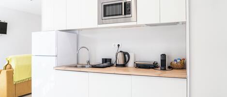 A modern kitchen with white cabinetry, a stainless steel microwave, a kettle, a toaster, and a sink.