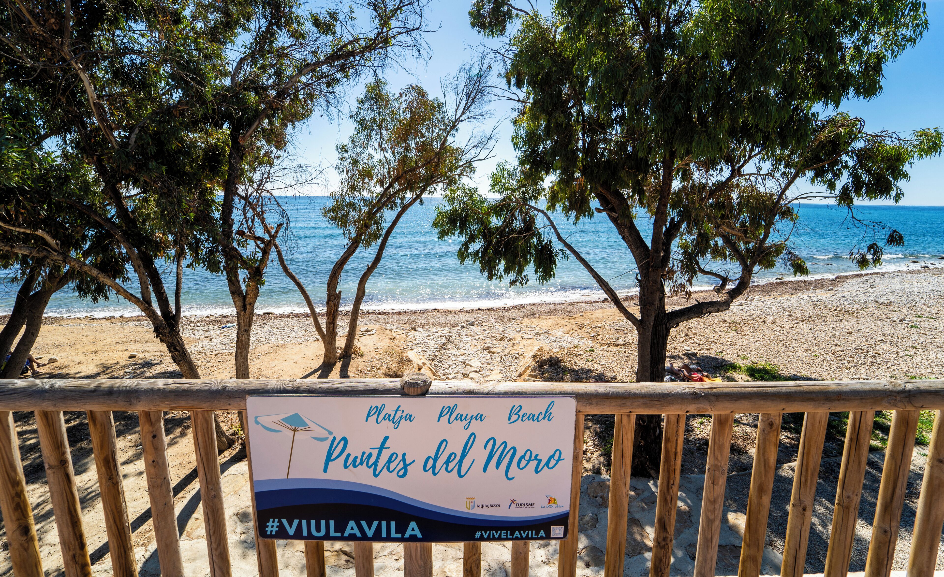 Et strandskilt med teksten "Playa Playa Beach Puntes del Moro" og hashtags #VIULAVILA og #VIVELAVILA.