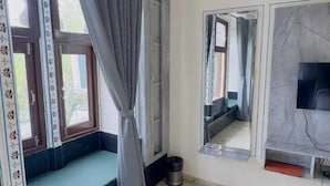 A room with a built-in bench, a large window with curtains, a mirror, and a television. - Hotel Moxa Inn (Udaipur)