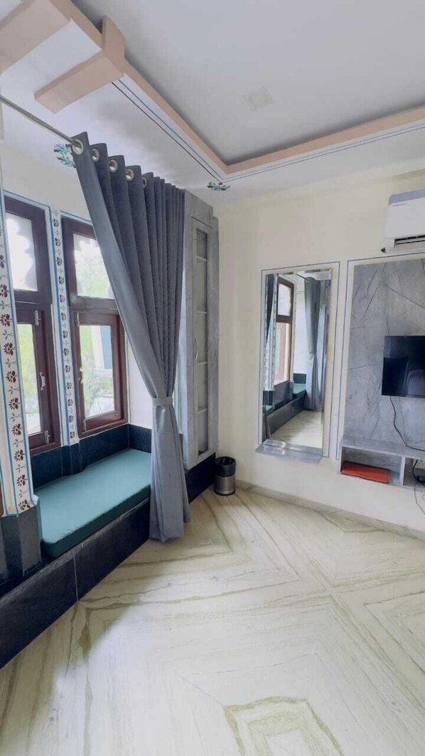 A room with a built-in bench, a large window with curtains, a mirror, and a television. - Hotel Moxa Inn (Udaipur)