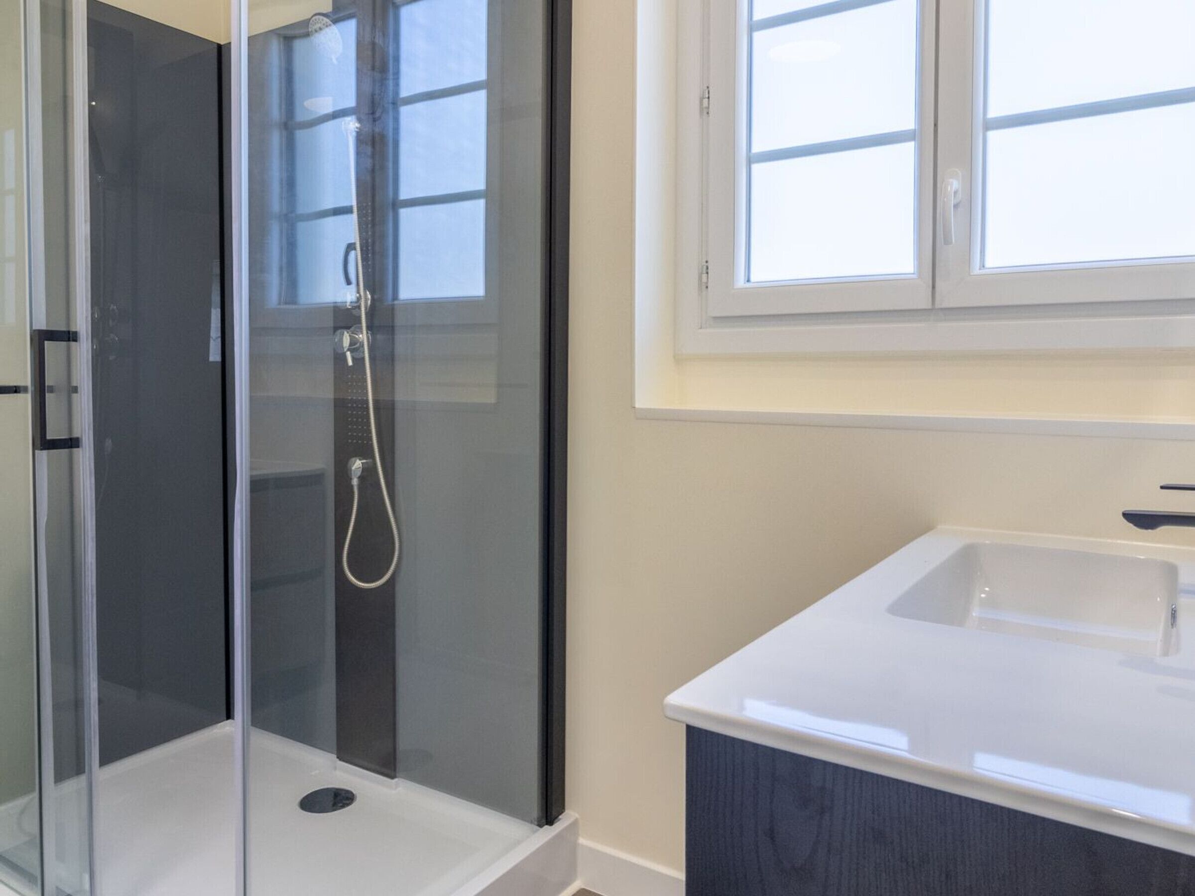 A bathroom with a glass-enclosed shower, a white sink, and a window above the sink.