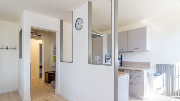 Eine moderne Wohnung mit Küche, Essbereich und Wohnzimmer. An der Wand befindet sich ein großer Spiegel, eine Uhr und ein Heizkörper.