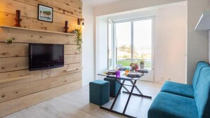 A modern living room with a wooden wall, a flat-screen TV, a dining table with chairs, and a large window. - Charming studio for 4 in Ciboure with terrace (Ciboure)