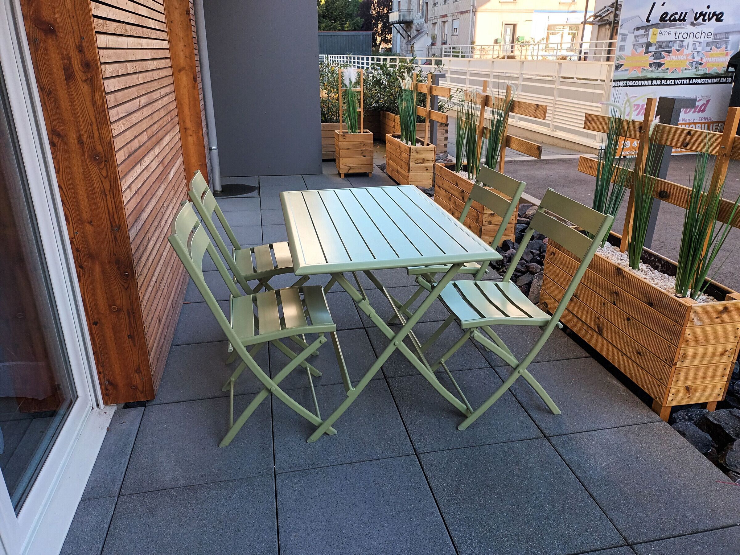 Ein grüner Metalltisch und -stühle auf einer gefliesten Terrasse mit Holz-Pflanzkästen und Pflanzen.