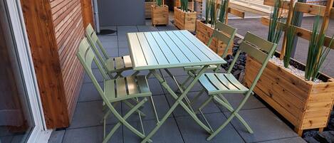 Ein grüner Metalltisch und -stühle auf einer gefliesten Terrasse mit Holz-Pflanzkästen und Pflanzen.