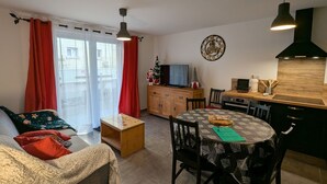 Ein gemütliches Wohnzimmer mit Sofa, Couchtisch und Fernseher. Es gibt einen Essbereich mit Tisch und Stühlen sowie eine Küche mit Herd und Schränken.