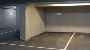 Eine Tiefgarage mit Betonwänden, einem dunklen Boden und einem einzigen beleuchteten Ausgangsschild.