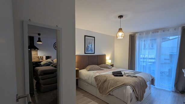 Ein modernes Schlafzimmer mit Bett, Nachttischen, einer Hängelampe und Blick ins Freie durch ein Fenster.