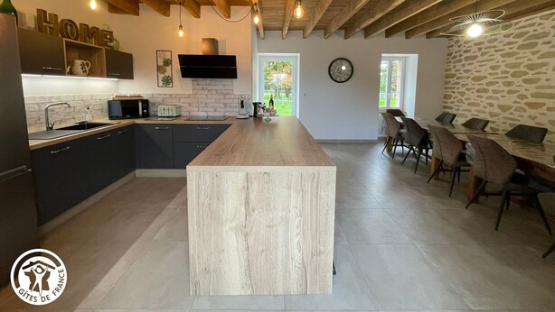 A modern kitchen with a central island, wooden ceiling beams, and a stone wall. - Family house with foosball and heated pool (Soullans)