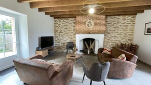 A living room with a stone fireplace, wooden ceiling beams, a television, and comfortable seating. - Family house with foosball and heated pool (Soullans)
