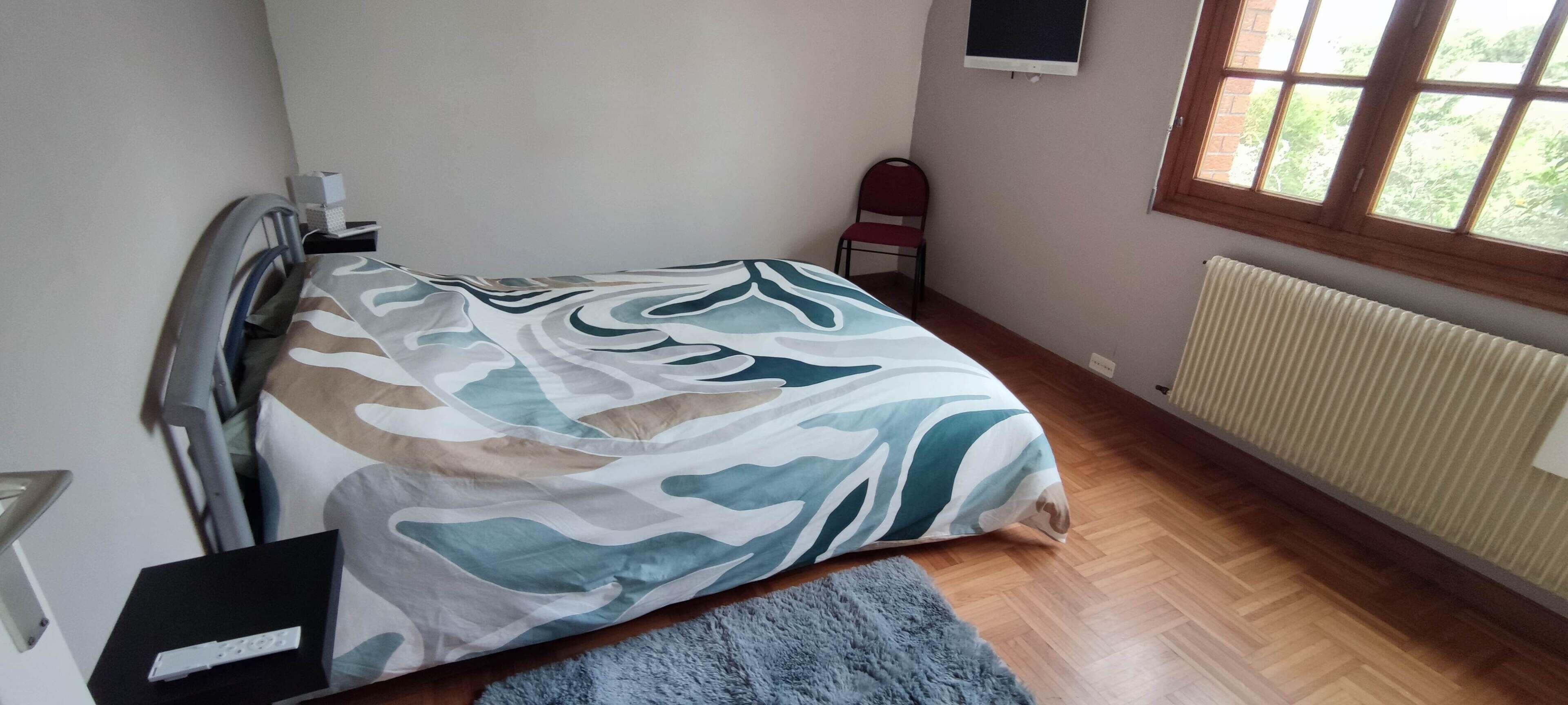 A bedroom with a bed, a chair, a radiator, and a window.