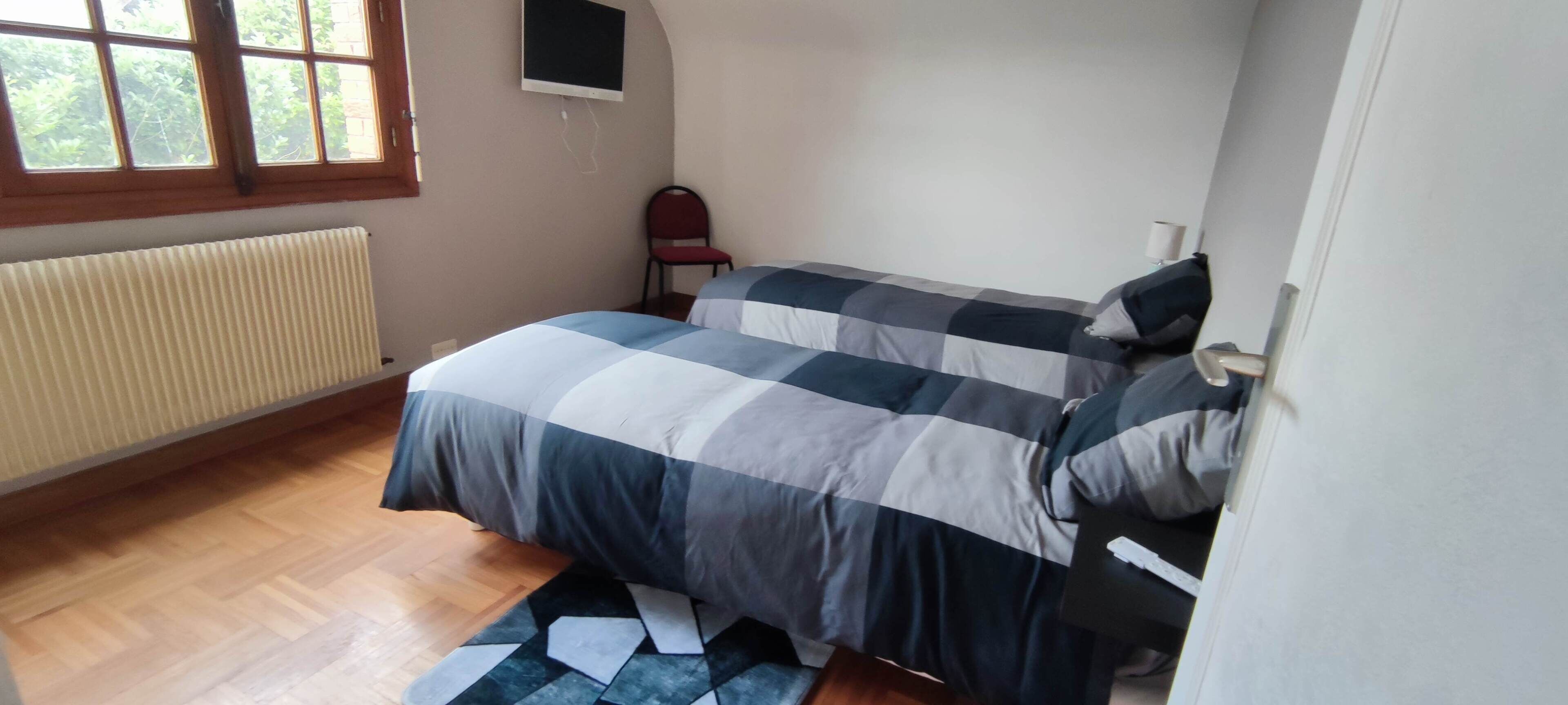 A bedroom with a bed, a chair, a radiator, and a window.
