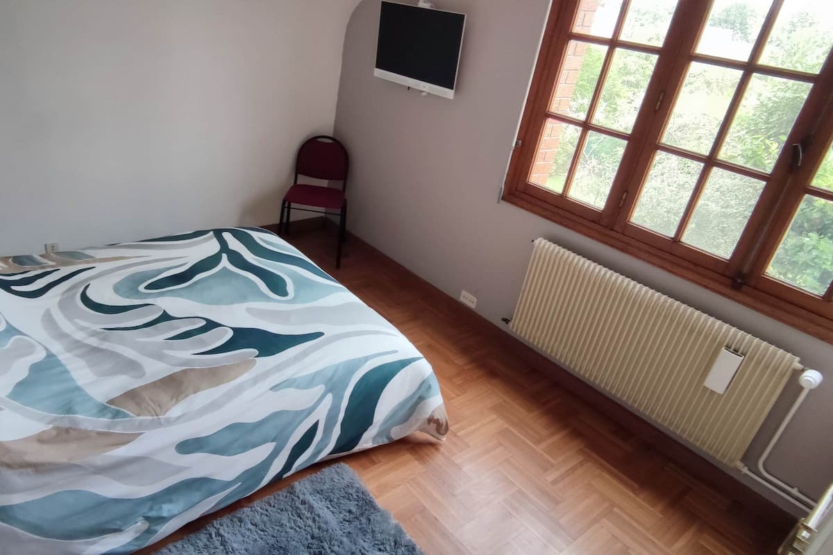 A bedroom with a bed, a chair, a TV, a window, and a radiator.