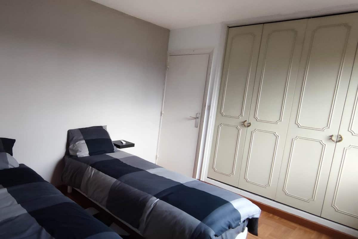 A bedroom with two beds, a wardrobe, and a bedside table with a lamp.