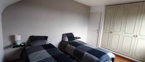 A bedroom with two beds, a wardrobe, and a bedside table with a lamp.