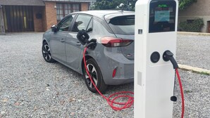 A gray car parked next to an electric vehicle charging station with a red cable connected. - L'Emmanuella (Isbergues)