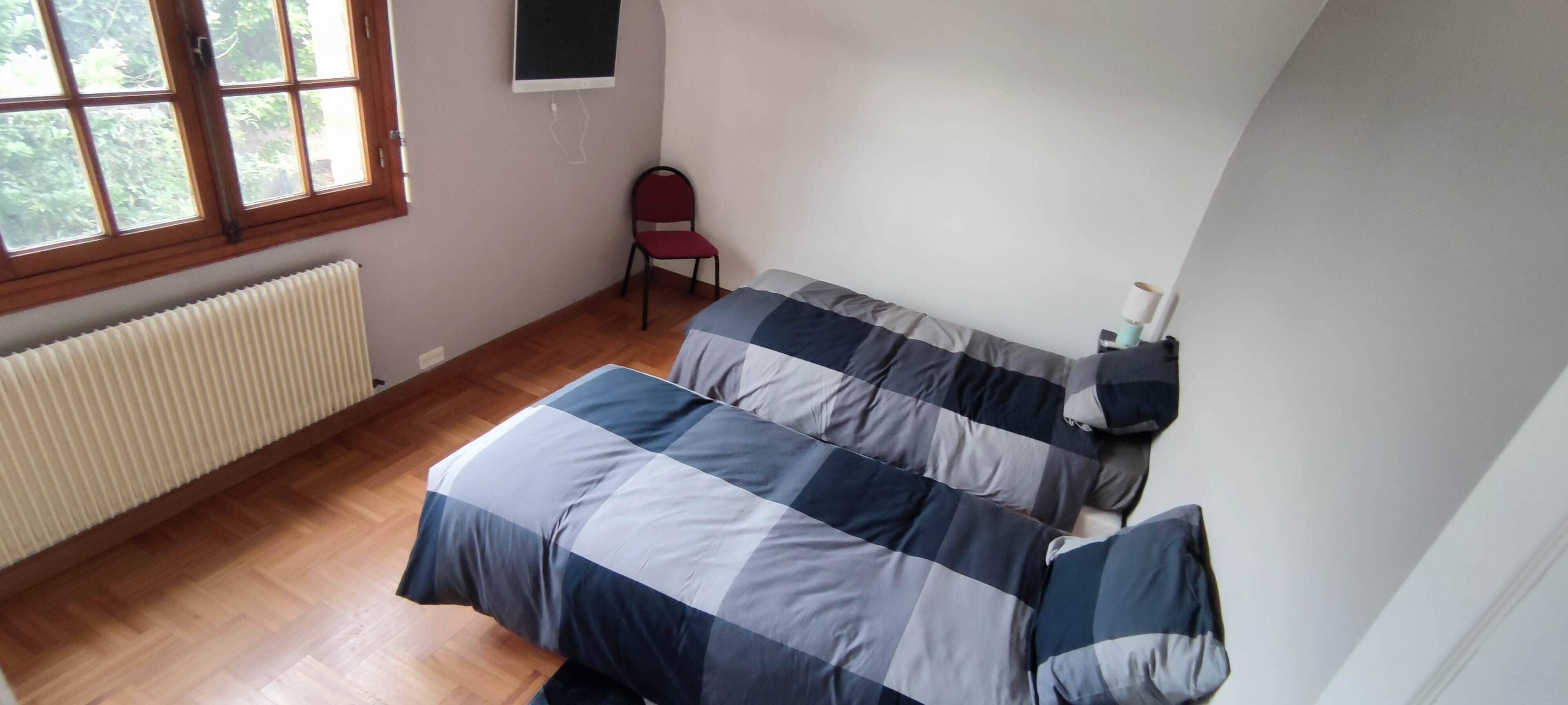 Un dormitorio con dos camas, un radiador, una ventana y una silla.