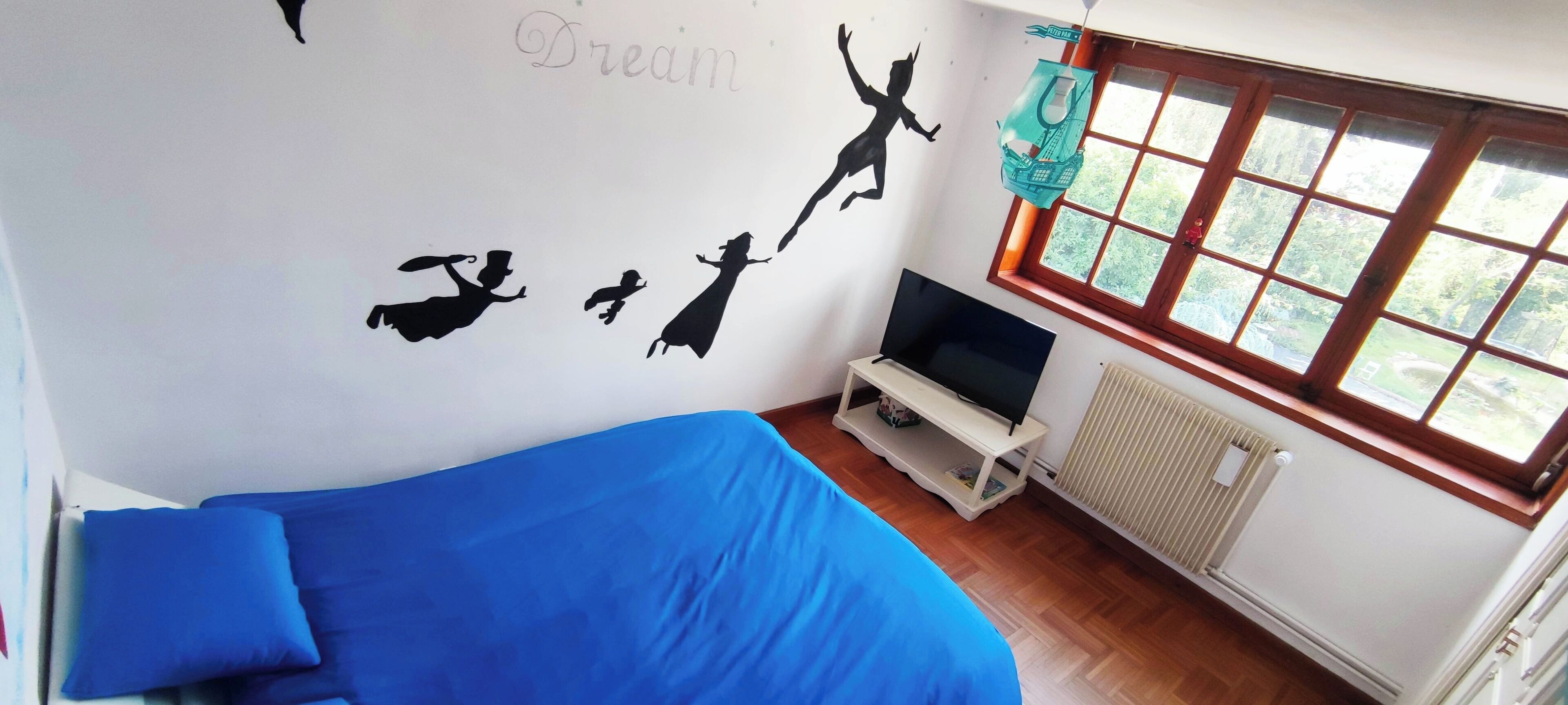 A room with a bed, a TV, a window, and a wall with silhouettes.