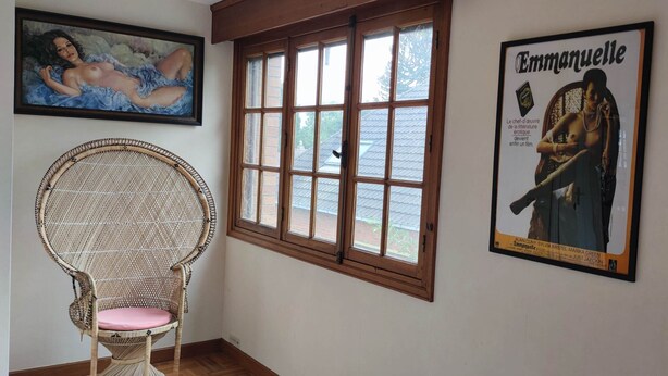 A room with a wicker chair, a large window, and two framed posters on the wall. - L'Emmanuella (Isbergues)