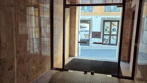Vue intérieure de l’entrée d’un hôtel, avec un sol carrelé et une porte en verre donnant sur l’extérieur.