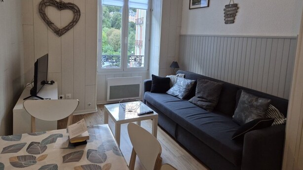Un salon chaleureux avec un canapé gris foncé, une table basse blanche et un objet décoratif en forme de cœur accroché au mur.