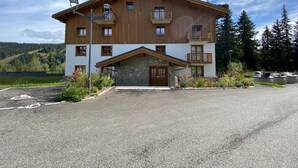 A two-story building with a stone entrance, multiple balconies, and a view of a forested area. - Comfortable apartment in Villard-sur-Doron for 6 people with parking (Villard-sur-Doron)