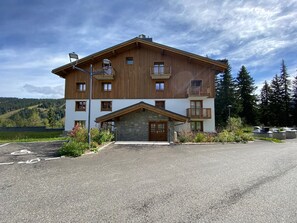 A two-story building with a stone entrance, multiple balconies, and a view of a forested area. - Comfortable apartment in Villard-sur-Doron for 6 people with parking (Villard-sur-Doron)