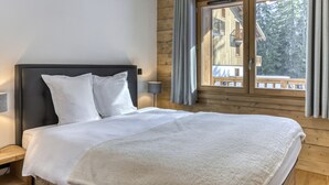 A bedroom with a bed, a nightstand, a window with curtains, and a view of a wooden building outside. - Comfortable apartment in Villard-sur-Doron for 6 people with parking (Villard-sur-Doron)