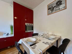 Un coin repas avec une table dressée pour quatre personnes, une cuisine rouge et un tableau encadré au mur.