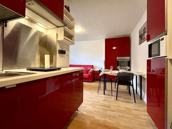 Une cuisine de taille réduite avec un coin repas, un canapé rouge et un four à micro-ondes.