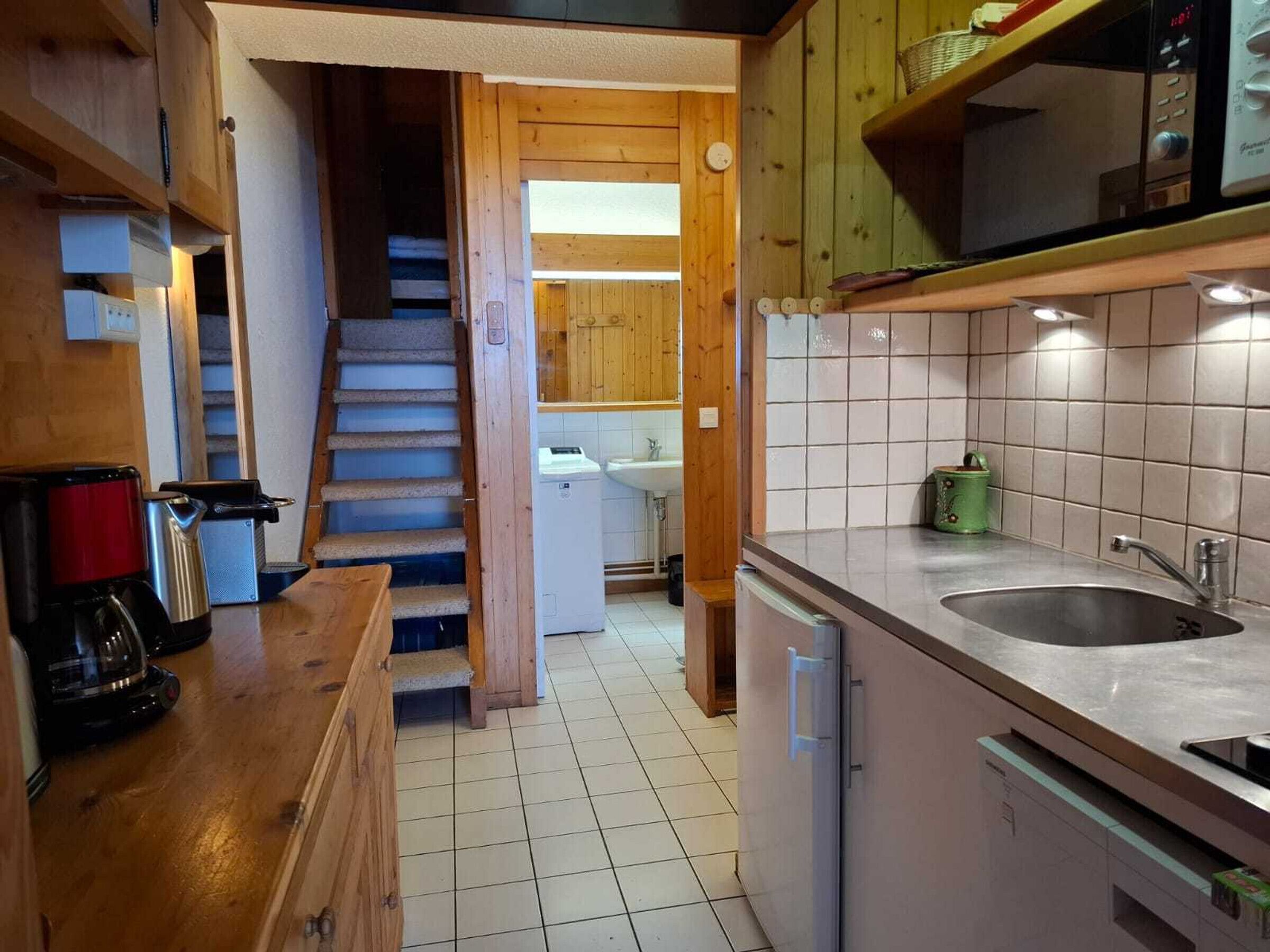 Una cocina compacta con armarios de madera, un lavamanos de acero inoxidable y una cafetera.