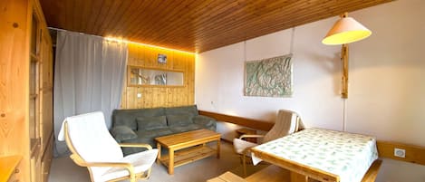 Una habitación acogedora con techo de madera, un sofá, una silla, una mesa y un banco.