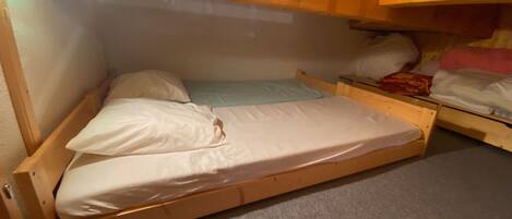 A small, single-bed room with a wooden bunk bed structure, a carpeted floor, and a ceiling light fixture.