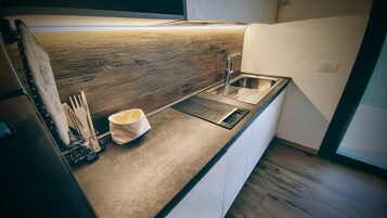 Una cocina moderna con protector de pared de madera, un lavamanos de acero inoxidable y un cubo de basura pequeño.
