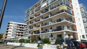 Un edificio residencial de varios pisos con balcones, una acera peatonal y automóviles estacionados.