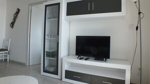 Una sala de estar moderna con un televisor de pantalla plana, un aparador con puertas de cristal y una mesa de centro blanca.