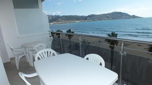 Un balcón con mesa y sillas blancas, con vista a una playa y el mar.