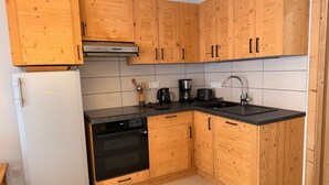 A compact kitchen with wooden cabinets, a built-in oven, a refrigerator, and a coffee maker. - Cozy apartment with large terrace and ski locker (Pralognan-la-Vanoise)