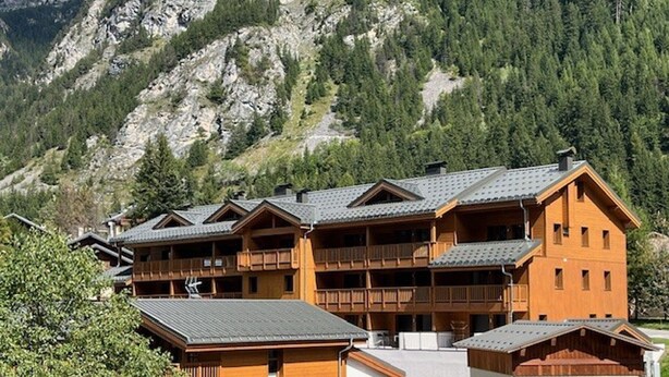 A multi-story wooden lodge with balconies, set against a mountainous backdrop. - Cozy apartment with large terrace and ski locker (Pralognan-la-Vanoise)