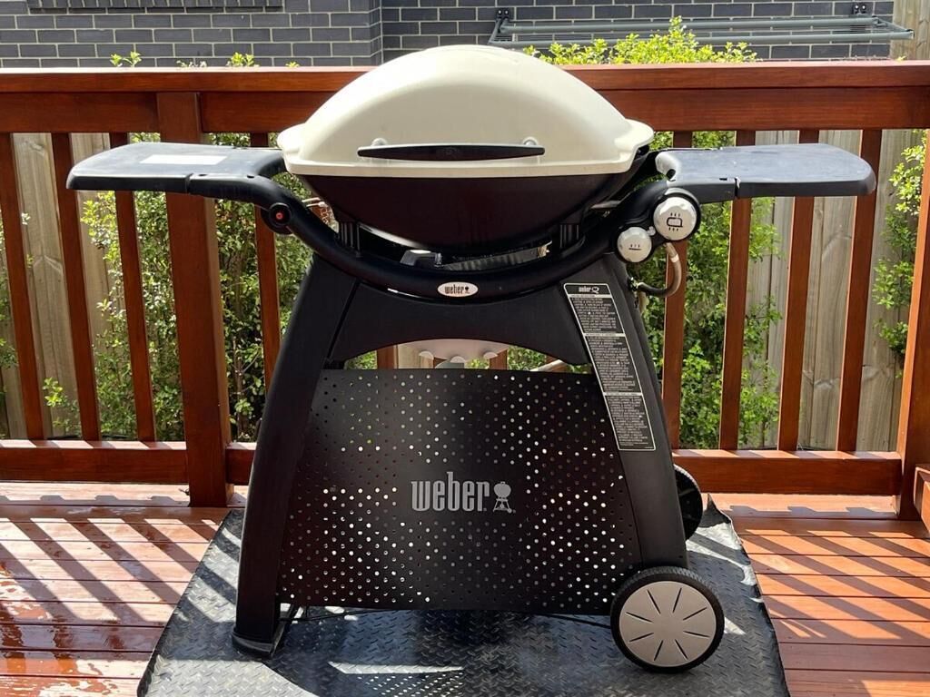 Un barbecue Weber portatif, muni de roulettes, posé sur une terrasse en bois.